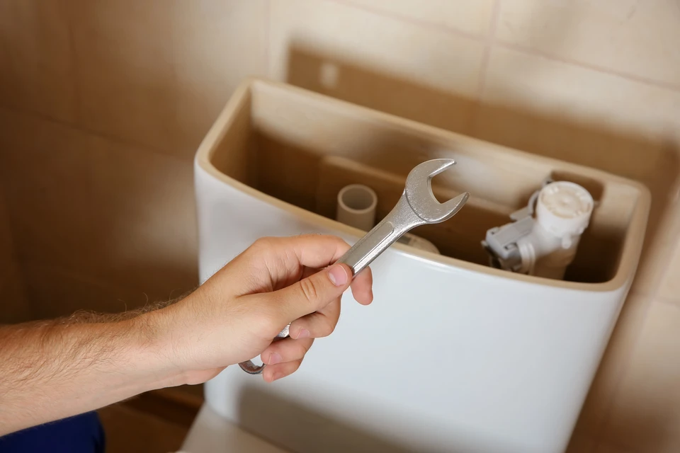 Main d'homme tenant une clé à molette dans une salle de bain, réparant le réservoir de chasse d'eau d'un WC