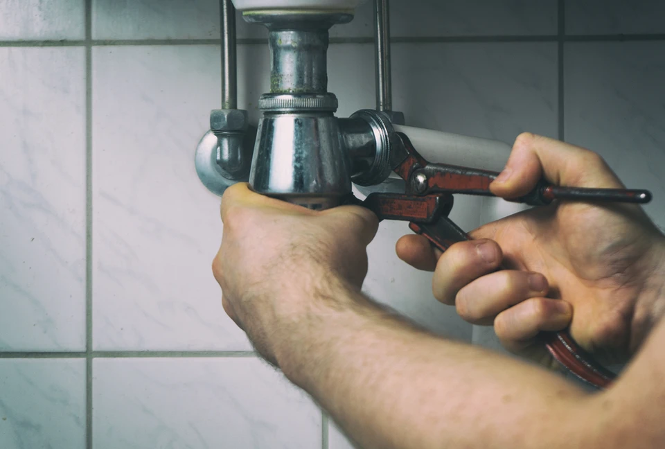 Intérieur salle de bain, mains masculines utilisant une clé à molette rouge pour serrer ou desserrer un raccord de plomberie sous lavabo