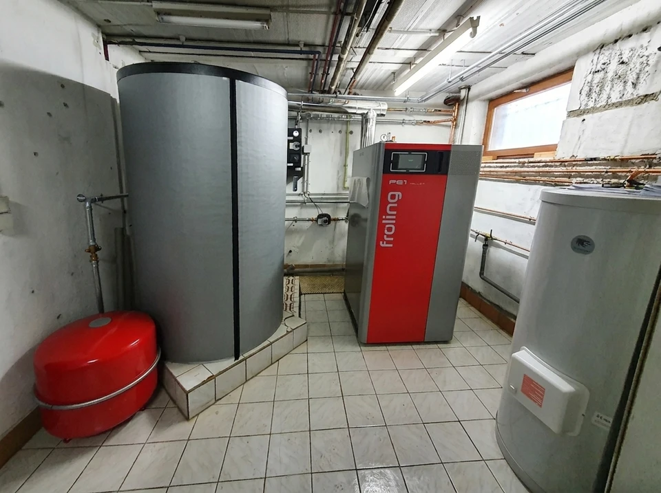 Extérieur résidentiel ensoleillé, pompe à chaleur air/air installée sur plots antivibratoires, fixée sur dalle béton, intégrée dans massif minéral avec gravier et arbustes ornementaux
