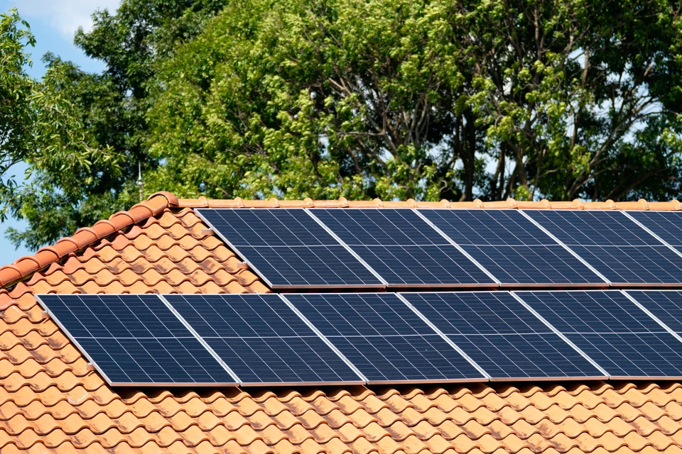 Une habitation moderne photographiée de côté, montrant simultanément sur son toit des panneaux solaires photovoltaïques (côté gauche) et une unité extérieure de pompe à chaleur air/air (côté droit ou en bas), illustrant visuellement la complémentarité entre énergies renouvelables et systèmes de chauffage modernes. La maison doit être clairement visible, bien entretenue, en lumière naturelle. Pas de texte ni logo.