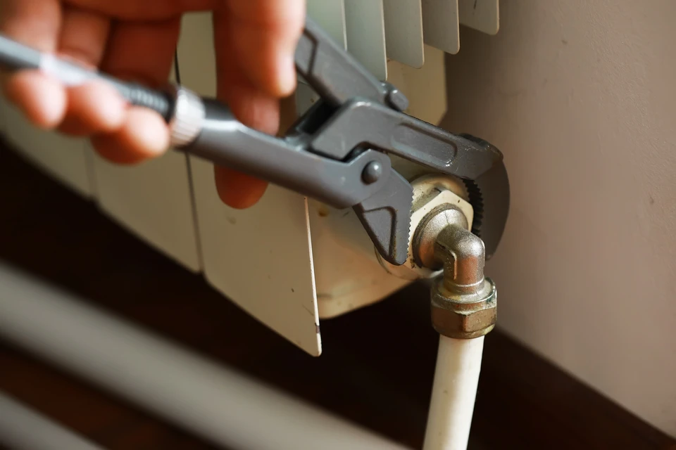 Homme en t-shirt gris ajustant un robinet thermostatique de radiateur dans un intérieur résidentiel