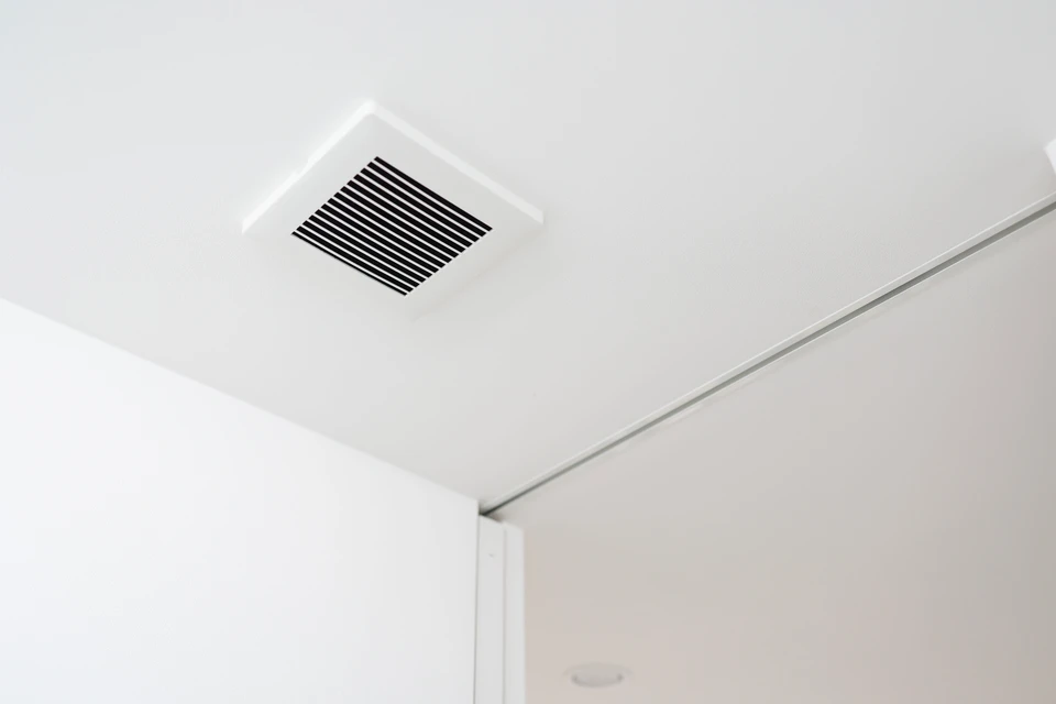 Photographie d'une pièce d'intérieur (salon ou cuisine) moderne et lumineuse, bien aérée, avec des surfaces claires et un air pur suggéré par la clarté et l'absence de condensation sur les vitres. La pièce doit paraître saine, confortable et accueillante, reflétant le bien-être apporté par une bonne ventilation. Si visible, une petite bouche d'extraction discrète de VMC peut être présente, intégrée naturellement à la décoration intérieure.
